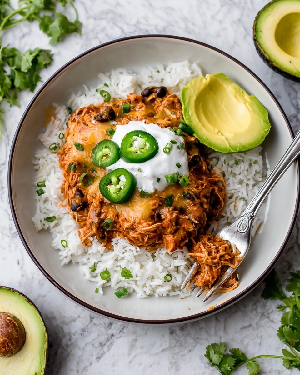 A white plate with a dark rim holds a bed of fluffy white rice as the first layer. On top, a thick layer of reddish-brown shredded chicken mixed with black beans and melted cheese is spread evenly. Three fresh green jalapeño slices sit on top, with chopped green herbs sprinkled over. A dollop of white sour cream covers part of the chicken layer. A bright green slice of avocado rests on the right side of the plate. A silver fork is placed partly on the rice. The plate is on a white marbled surface with a halved avocado and some green herbs nearby. photo taken with an iphone --ar 4:5 --v 7