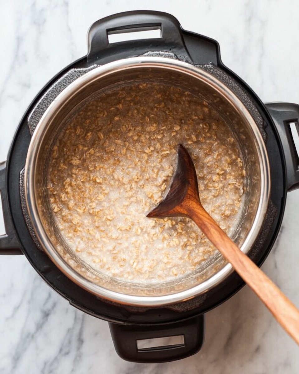A close-up top view of a black electric pressure cooker with a shiny silver inner pot filled with cooked oatmeal. The oatmeal is light brown with a thick, creamy texture, and a wooden spoon with a long brown handle is stirring the oatmeal from the right side of the pot. The cooker is placed on a white marbled surface photo taken with an iphone --ar 4:5 --v 7