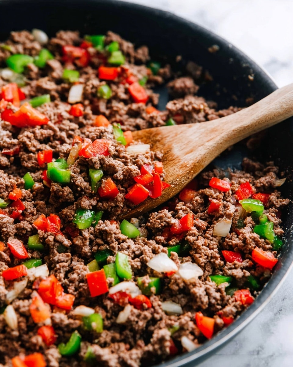 A close-up view of a black frying pan filled with cooked ground beef mixed with diced red and green bell peppers and small chunks of white onion, creating a colorful mix of brown, bright red, green, and white pieces. A wooden spoon rests inside the pan, slightly lifting some of the mixture, showing the textures of crumbly beef and crisp vegetables. The pan sits on a white marbled surface, enhancing the vibrant colors of the food. photo taken with an iphone --ar 4:5 --v 7