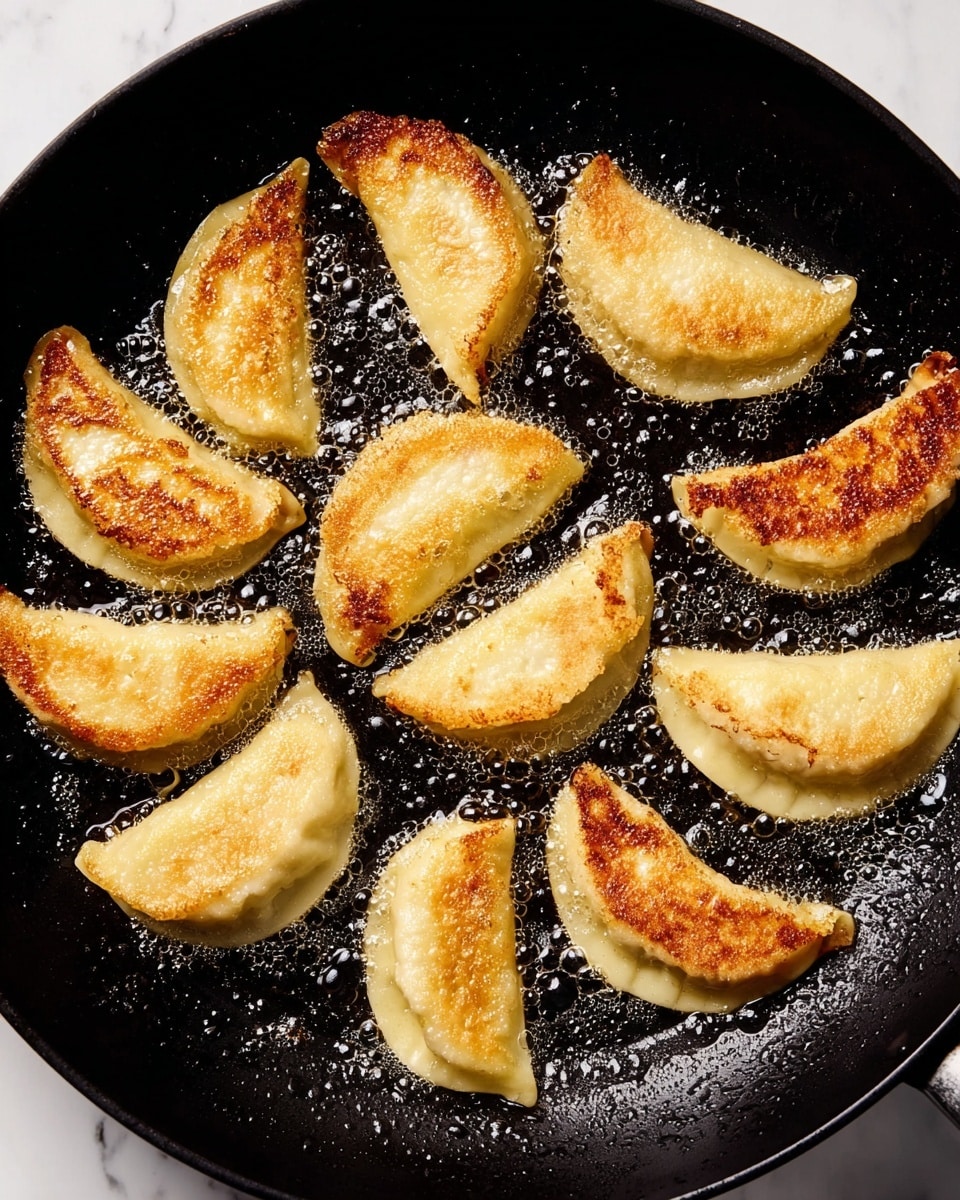 There are eleven half-circle dumplings frying in a black pan. Each dumpling has a light golden color with a crispy, browned texture on the top side, showing small spots of dark caramelization. The edges are pale and soft, while the browned parts look slightly rough and crunchy. The pan holds a small amount of bubbling oil, giving a shiny gloss to the dumplings. The background is a white marbled surface, and no woman's hand is visible. photo taken with an iphone --ar 4:5 --v 7