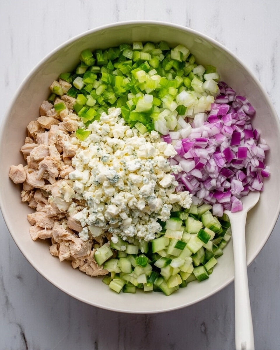 The image shows a white bowl on a white marbled surface, filled with several layers of ingredients arranged separately. Starting from the left side, there is chopped light brown cooked chicken, followed by bright green small celery pieces next to it. Toward the top right, there are small diced green cucumbers with a fresh texture. To the right center, there is a large mound of crumbly white cheese. At the bottom, purple chopped red onions form a colorful layer. A white spatula is placed off to the right side of the bowl. The photo taken with an iphone --ar 4:5 --v 7