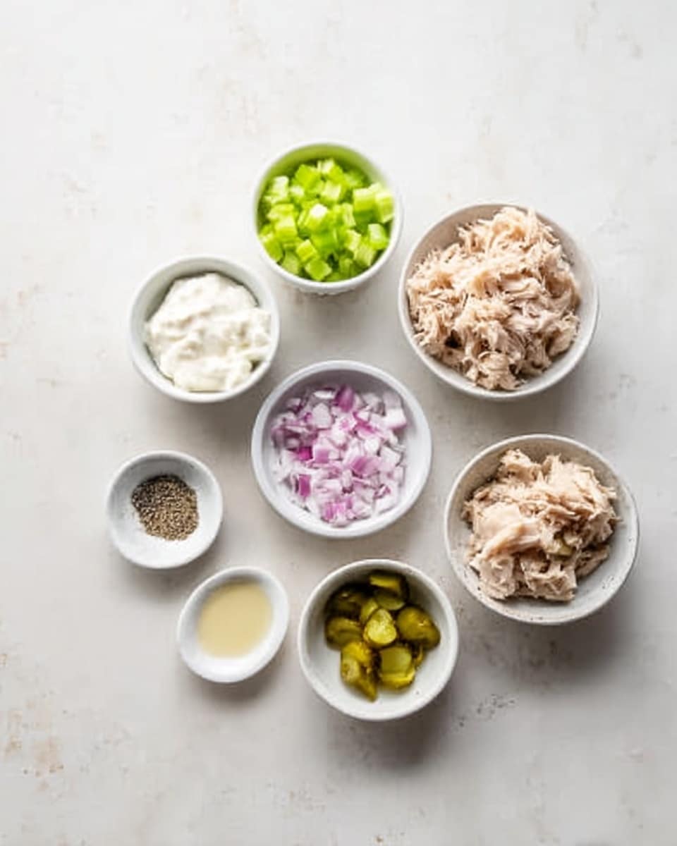 Seven small white bowls and dishes placed on a white marbled surface, each containing different ingredients: the top left bowl has a white creamy substance, next to it on the right is a bowl with bright green chopped celery, followed by a bowl to the right filled with light beige shredded meat. Below, starting from the left, a small bowl holds finely chopped red onion, next to it is a bowl with yellowish-green chopped pickles, below these two are three small dishes—one with mixed black and white pepper, one with a small dollop of mustard, and the last one with a pale liquid. The bowls and dishes are neatly arranged in a casual semi-circle pattern. photo taken with an iphone --ar 4:5 --v 7