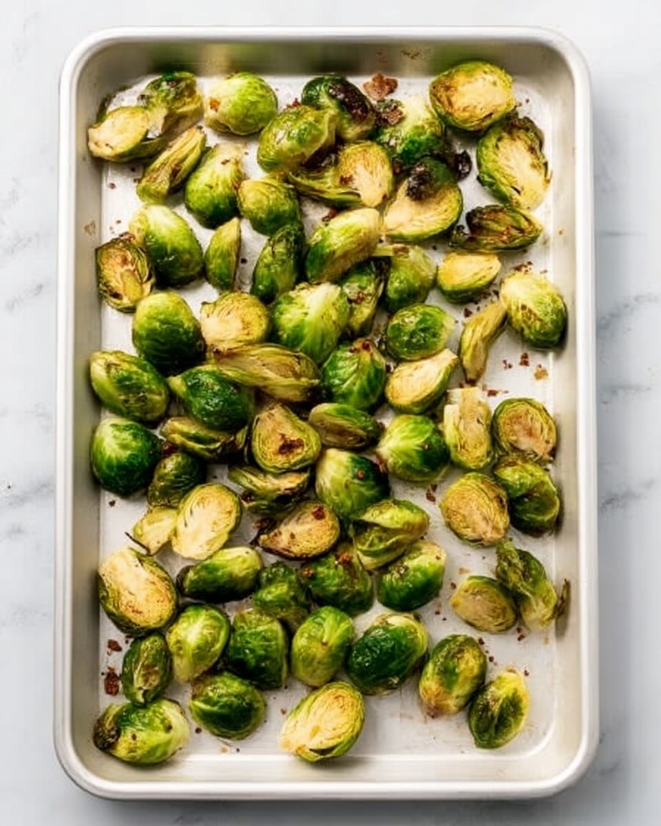 A white tray filled with roasted Brussels sprouts, some whole and some halved, spread evenly across the surface. The Brussels sprouts are bright green with slight brown edges indicating roasting, and some pieces show a soft texture inside. The tray is on a white marbled surface, providing a clean and simple background. photo taken with an iphone --ar 4:5 --v 7