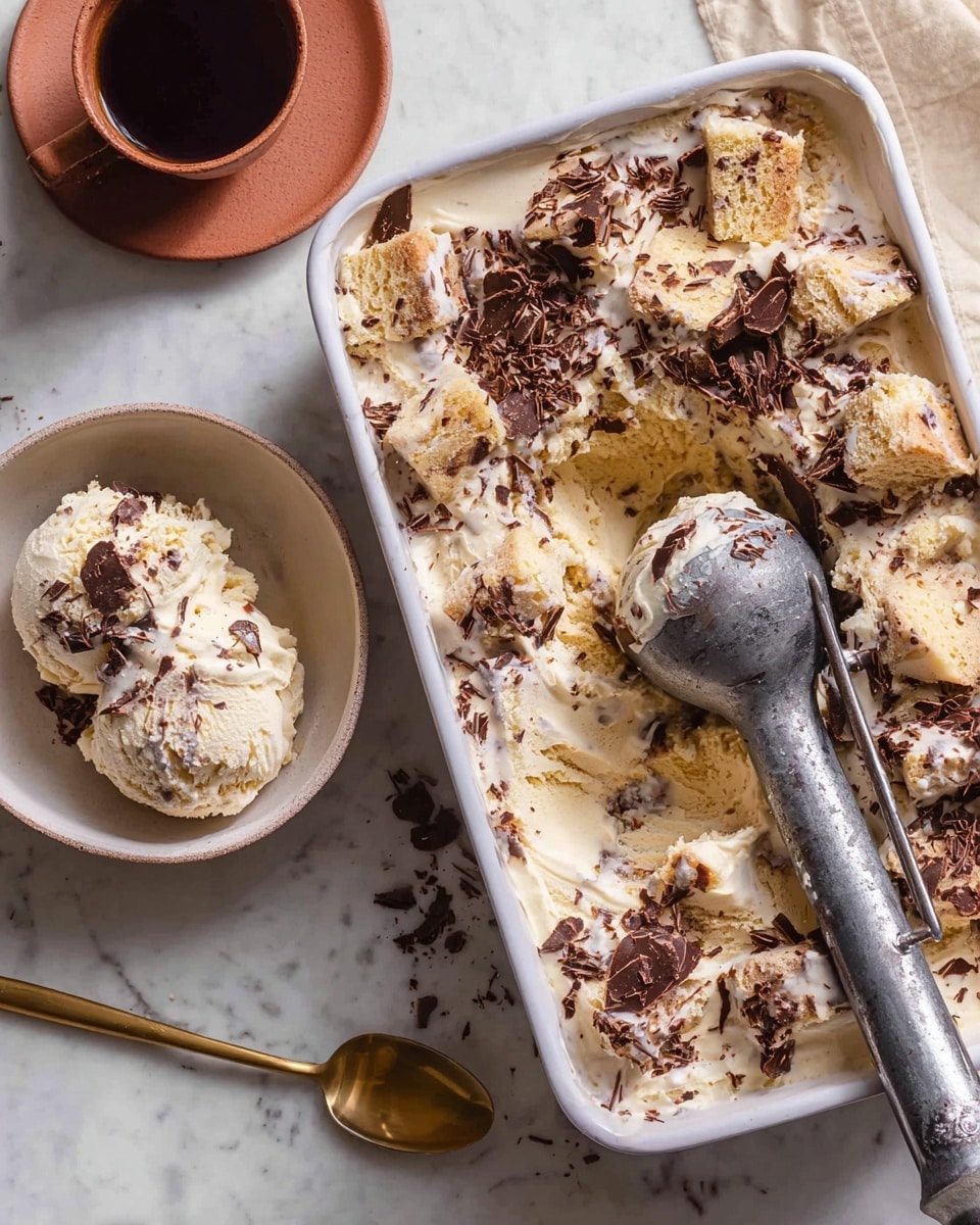 A white rectangular dish holds layers of creamy ice cream mixed with light beige cake pieces, topped with dark chocolate shavings scattered unevenly. A large vintage metal ice cream scooper rests inside the dish, partially filled. To the left, there is a white bowl with a single round scoop of the same ice cream, showing textures of cake bits and chocolate shavings, with a golden spoon next to it. The setting is on a white marbled surface, with a brown cup containing coffee in the top left corner. photo taken with an iphone --ar 4:5 --v 7