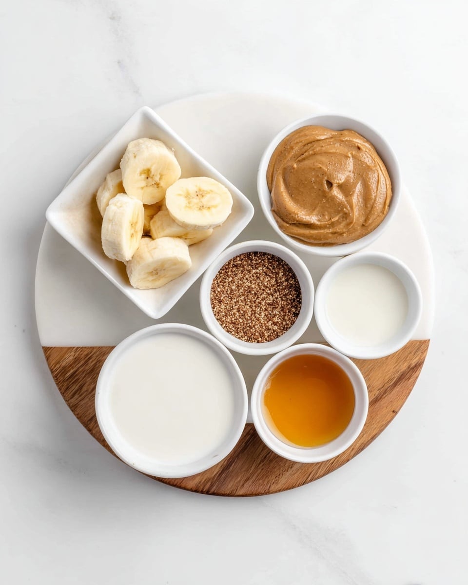 The image shows a white round plate with a wood edge placed on a white marbled surface. On the plate, there are five small white bowls arranged in a circular shape. Starting from the top right, there's a bowl filled with smooth brown peanut butter. To the left of this bowl, a square white bowl holds thick slices of pale yellow banana. Below the peanut butter, a small white bowl contains a coarse brown powder, likely ground flaxseed. Directly below the flaxseed, another bowl is filled with white liquid, probably some type of milk. At the bottom right corner of the plate, a small bowl holds a golden amber liquid, possibly honey or syrup. The layout is neat and all items are clearly visible. photo taken with an iphone --ar 4:5 --v 7