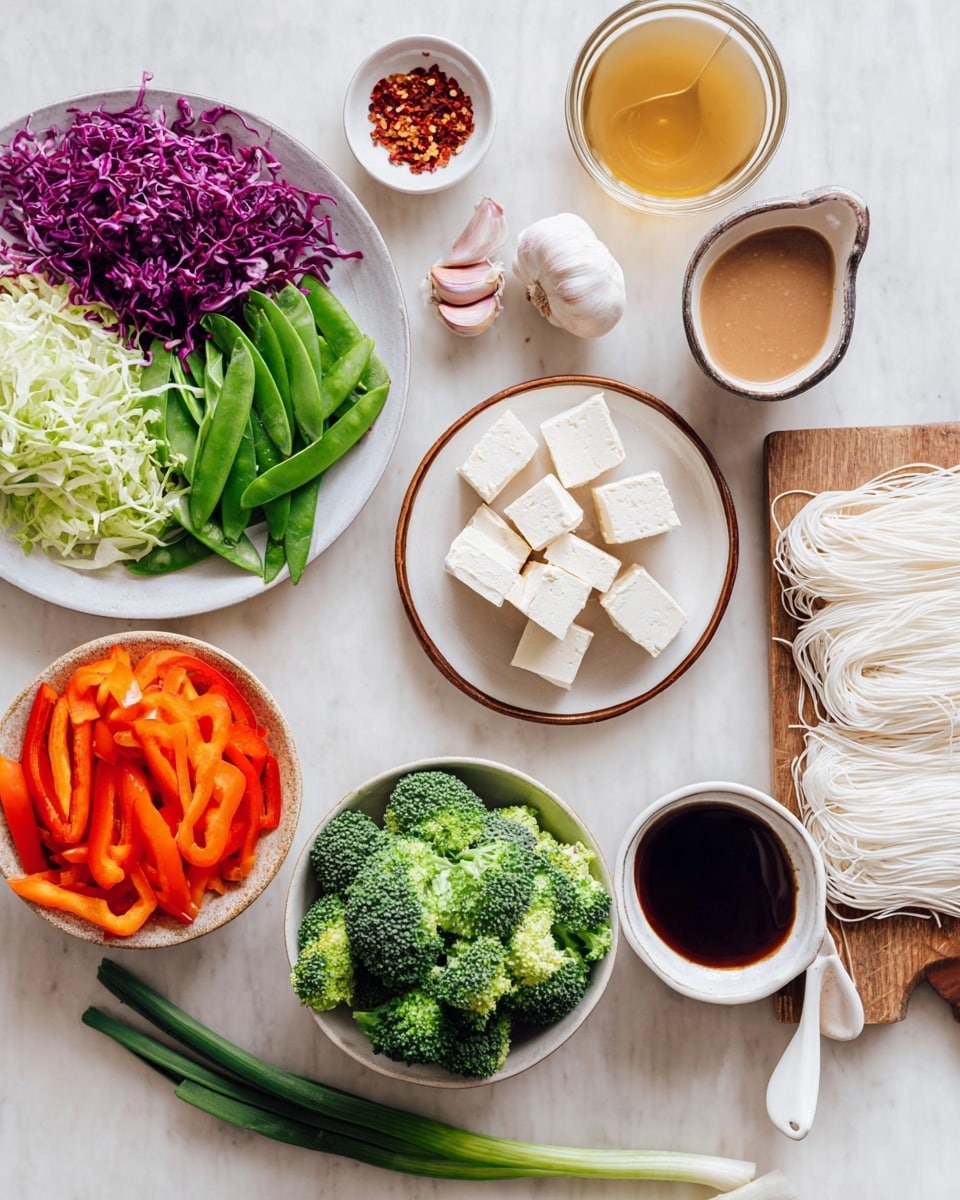 The image shows a neatly arranged top-down view of fresh ingredients on a white marbled surface. There is a white plate on the left side filled with colorful vegetables: shredded purple cabbage at the top, bright green snap peas in the middle, light green leafy greens at the bottom left, and vibrant orange bell pepper slices on the right. Below that, a round bowl holds bright green broccoli florets. Moving upward, cubes of light beige tofu are stacked on a white plate with a brown rim near the upper left corner. To the right of the tofu, two whole garlic cloves rest on the surface. Next to them, a white ceramic spoon holds red chili flakes, and above that is a small white bowl with golden liquid. On the right side, thin white noodles are neatly spread over a wooden board. At the bottom right corner, a small white bowl contains dark soy sauce, and beside it is a glass cup filled with creamy peanut sauce with a white ceramic spoon inside. Two fresh green onions lie diagonally near the center. Photo taken with an iphone --ar 4:5 --v 7