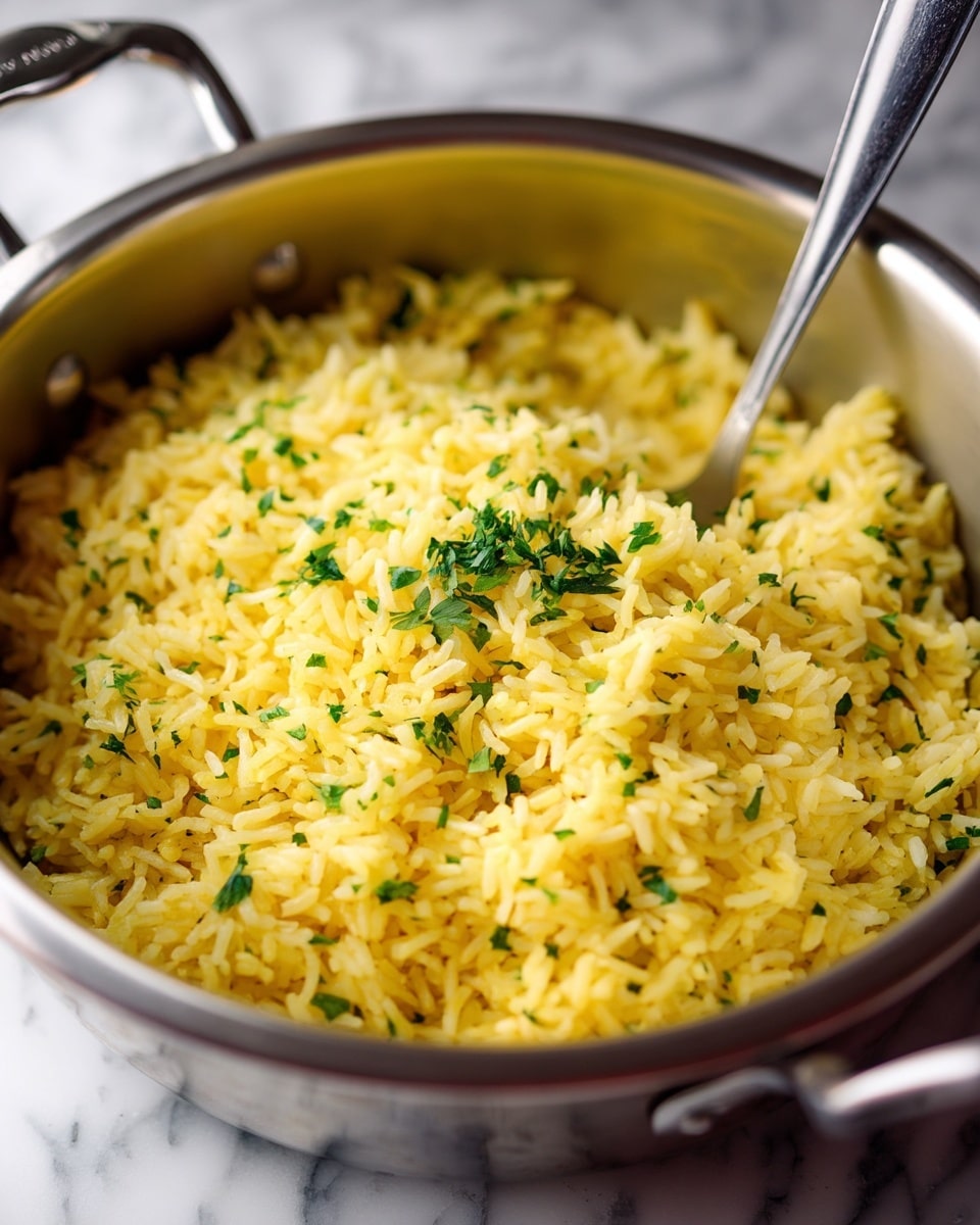 A large silver cooking pot is filled with yellow rice mixed with small green herb pieces scattered evenly throughout. A metal spoon stands upright in the rice, reflecting light softly. The rice grains are fluffy and separate, with a light texture visible on each grain. The pot's inside surface is smooth and shiny, contrasting with the rice texture. The background shows part of a white marbled surface and a stove edge in black and silver tones. photo taken with an iphone --ar 4:5 --v 7