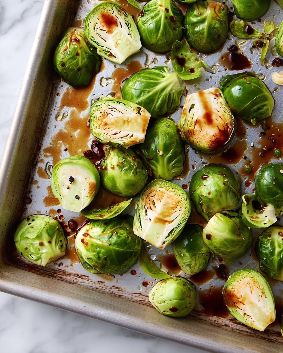 The image shows many Brussels sprouts spread out on a metal baking sheet on a white marbled surface. The Brussels sprouts are halved and whole, with bright green, crinkled outer leaves and pale yellow inner layers visible in the cut pieces. There are dark brown sauce drips and small black pepper bits scattered over the Brussels sprouts and baking sheet, giving a glossy look on some parts. The texture of the Brussels sprouts is fresh and slightly shiny from the sauce, creating a mix of rough leafy surfaces and smooth cut edges. Photo taken with an iphone --ar 4:5 --v 7
