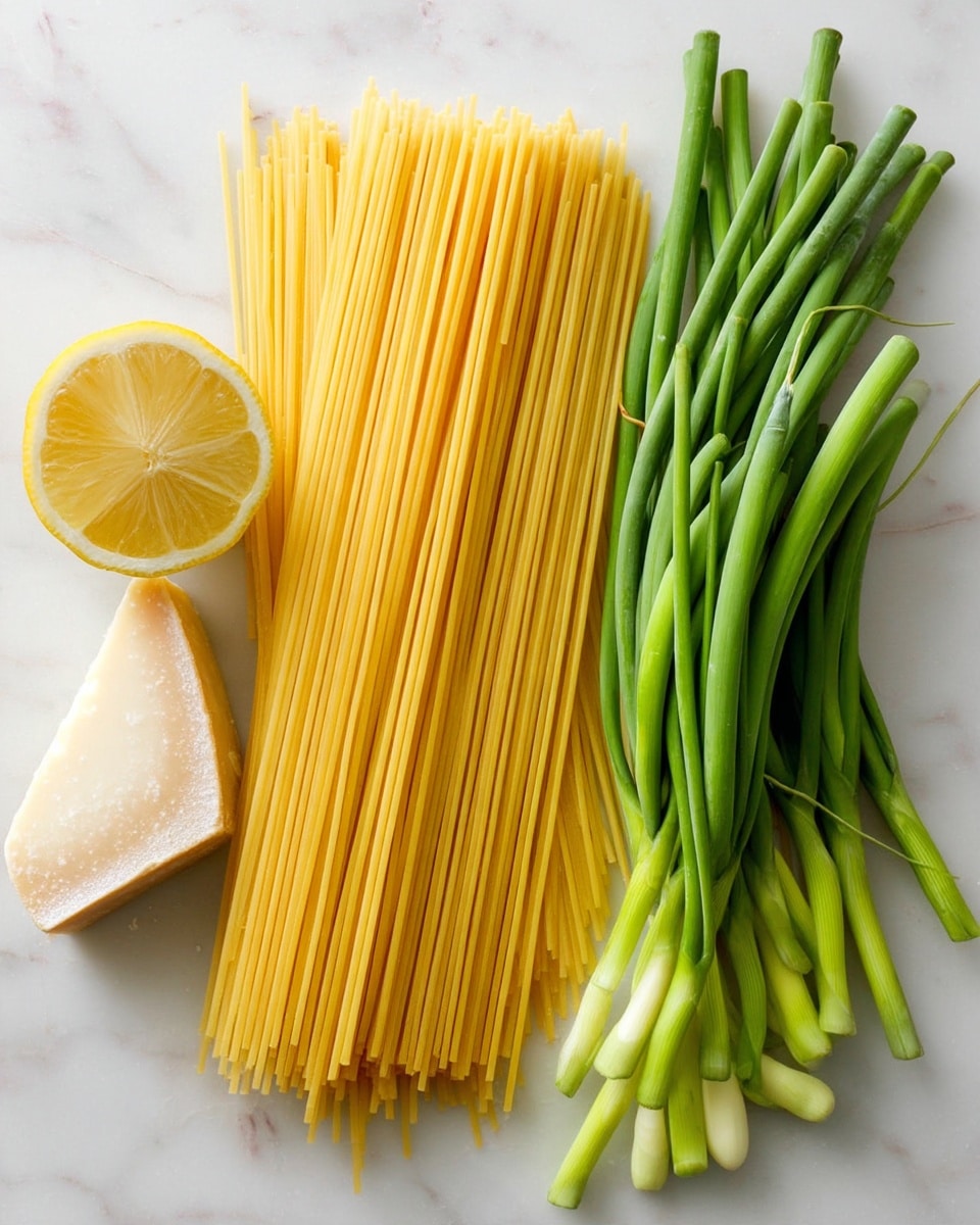 The image shows long yellow uncooked spaghetti arranged neatly on the right side of a white marble surface. To the left, there are two bunches of curled green garlic scapes stacked loosely, with their light green and white ends visible. Above the bottom bunch, there is a half lemon showing its pale yellow inside. At the bottom left corner, there is a piece of hard cheese with a rough and grainy texture placed flat. The overall colors are soft and natural, with a clean and fresh look. Photo taken with an iphone --ar 4:5 --v 7