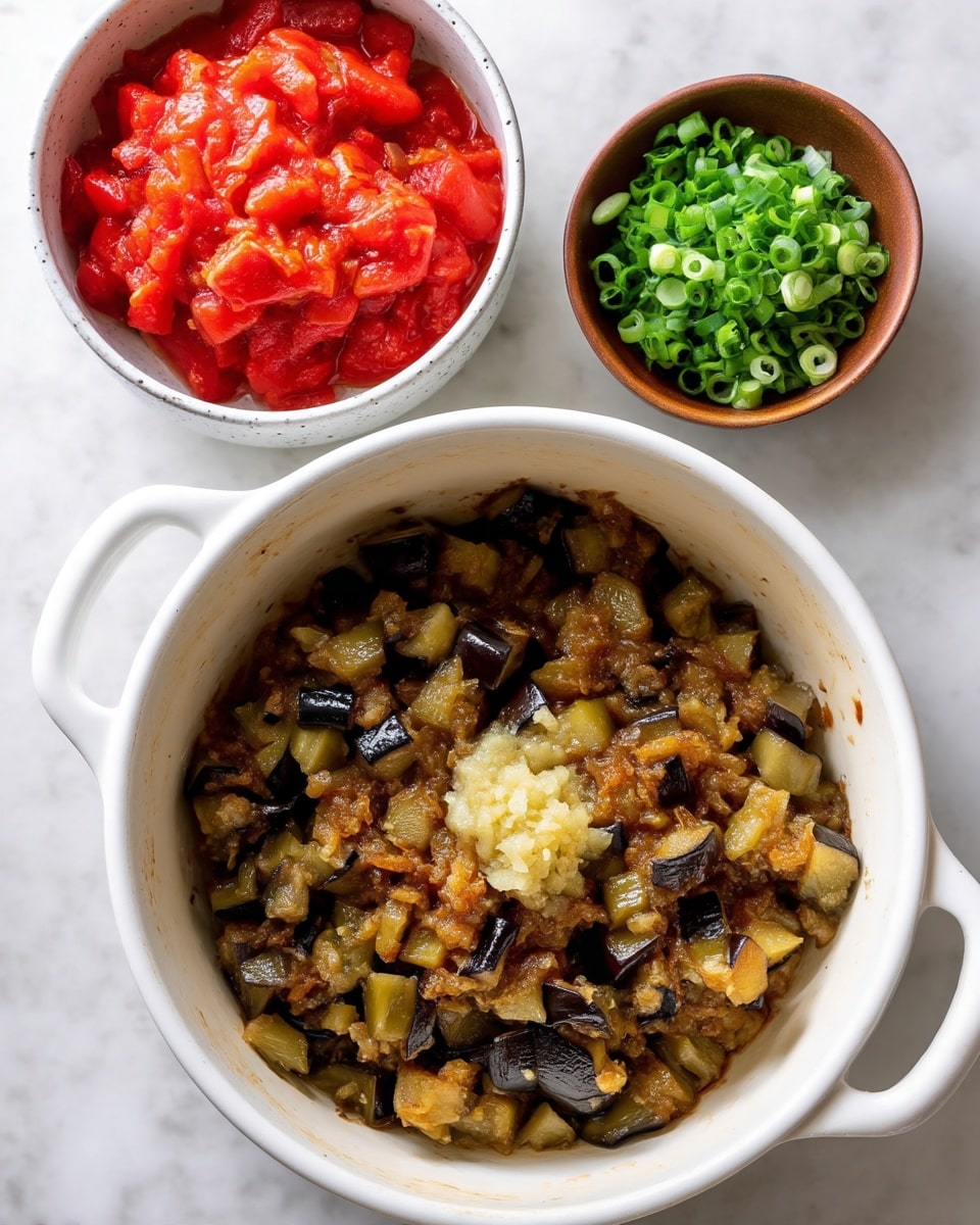 A white pot with two handles holds a cooked mixture of small green and dark purple eggplant pieces, some browned bits around the edge showing a light oily texture, with a small mound of finely minced pale yellow garlic placed in the center on top. Above and to the left, a white bowl filled with chunky bright red diced tomatoes in juice sits on a white marbled surface. Below and to the right, a small brown bowl contains chopped green onions. photo taken with an iphone --ar 4:5 --v 7